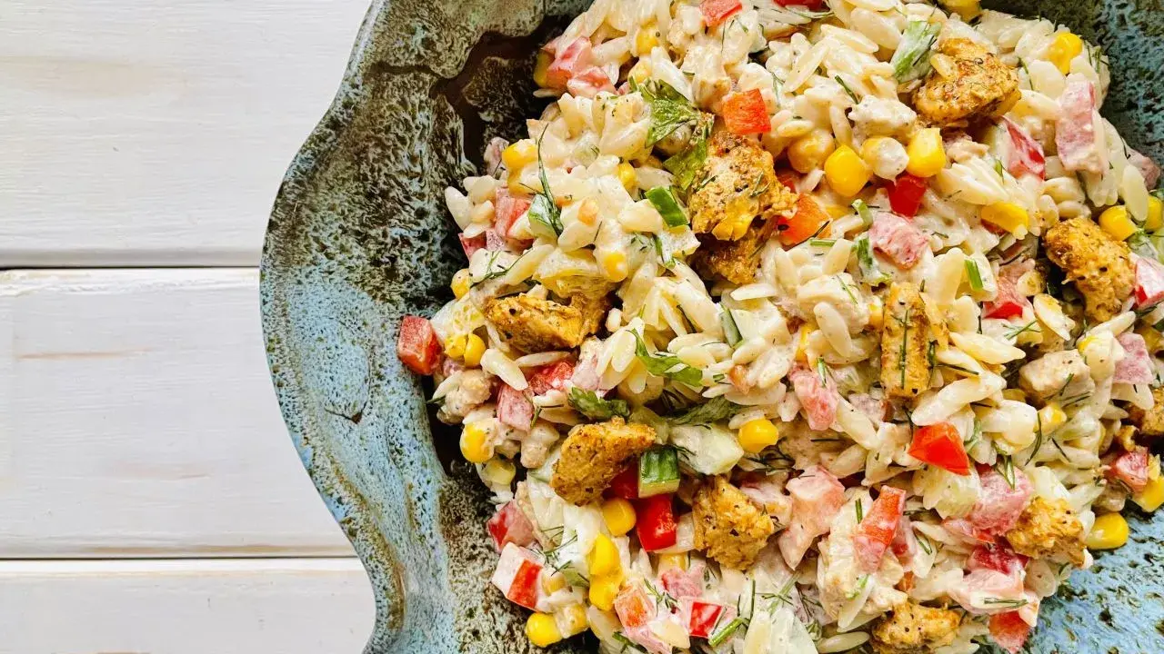 Pyszna sałatka z makaronem orzo i kurczakiem, z dodatkiem kukurydzy, papryki i ziół, podana w ceramicznej misie.