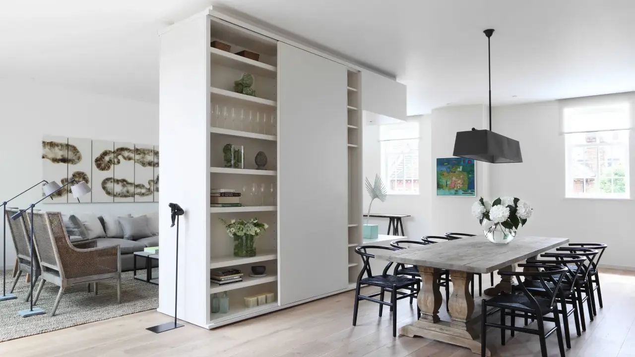 En vit rumsavdelare etta med hyllor delar av ett modernt vardagsrum och matplats.