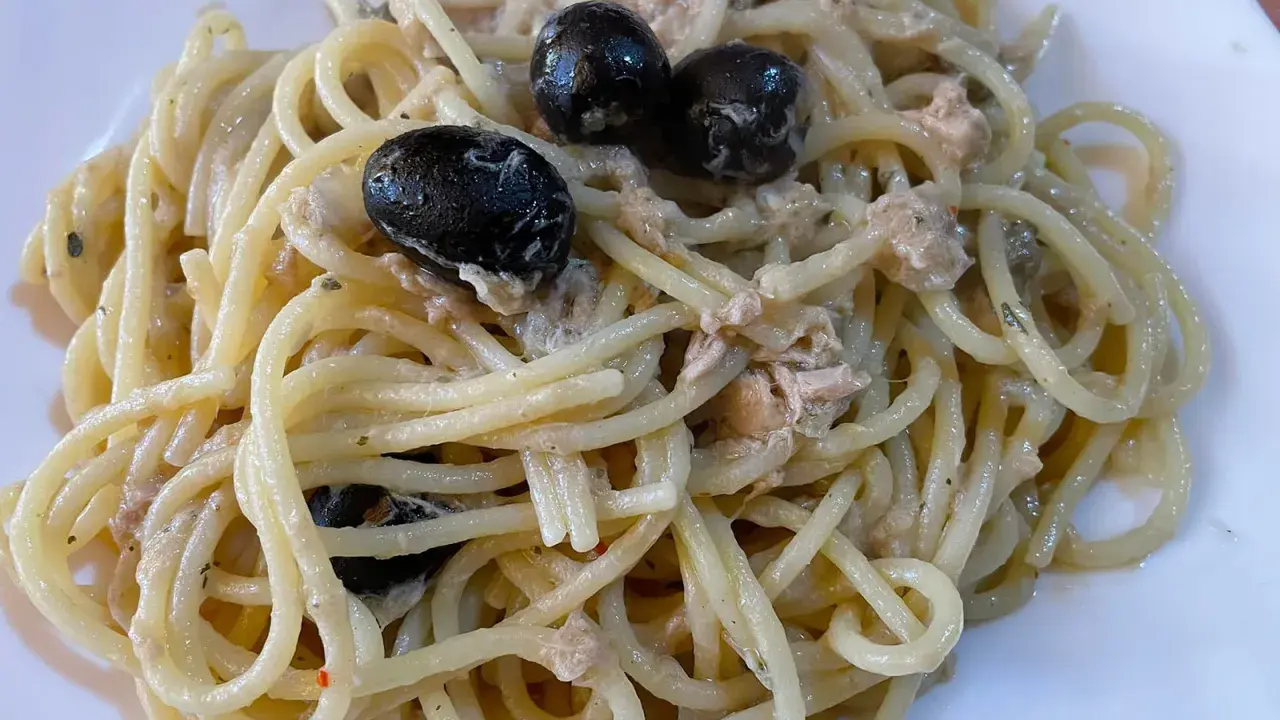 Un piatto di spaghetti conditi con tonno e olive nere, un classico della cucina italiana.