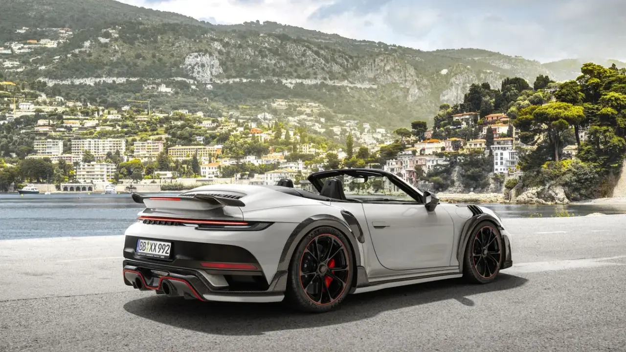 Ein weißer Techart GTstreet RS Cabriolet steht an einer Küstenstraße mit Blick auf eine malerische Stadt am Hang.