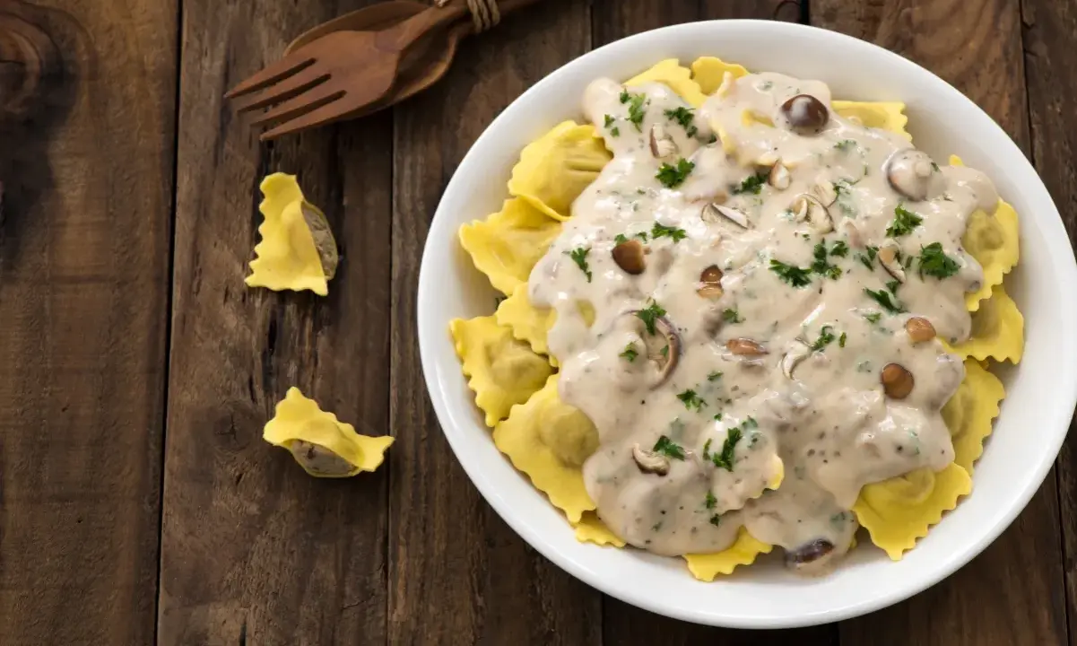 Ravioli w kremowym sosie śmietanowym z grzybami i natką pietruszki, podane na drewnianym stole.