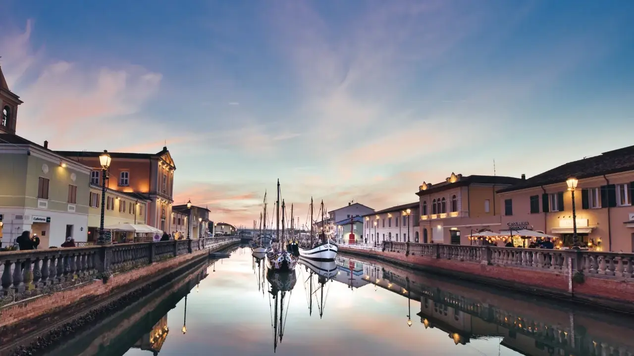 Canale di Cesenatico al tramonto, con barche a vela ormeggiate e riflessi sull'acqua. La riviera cesenatico incanta con i suoi colori.