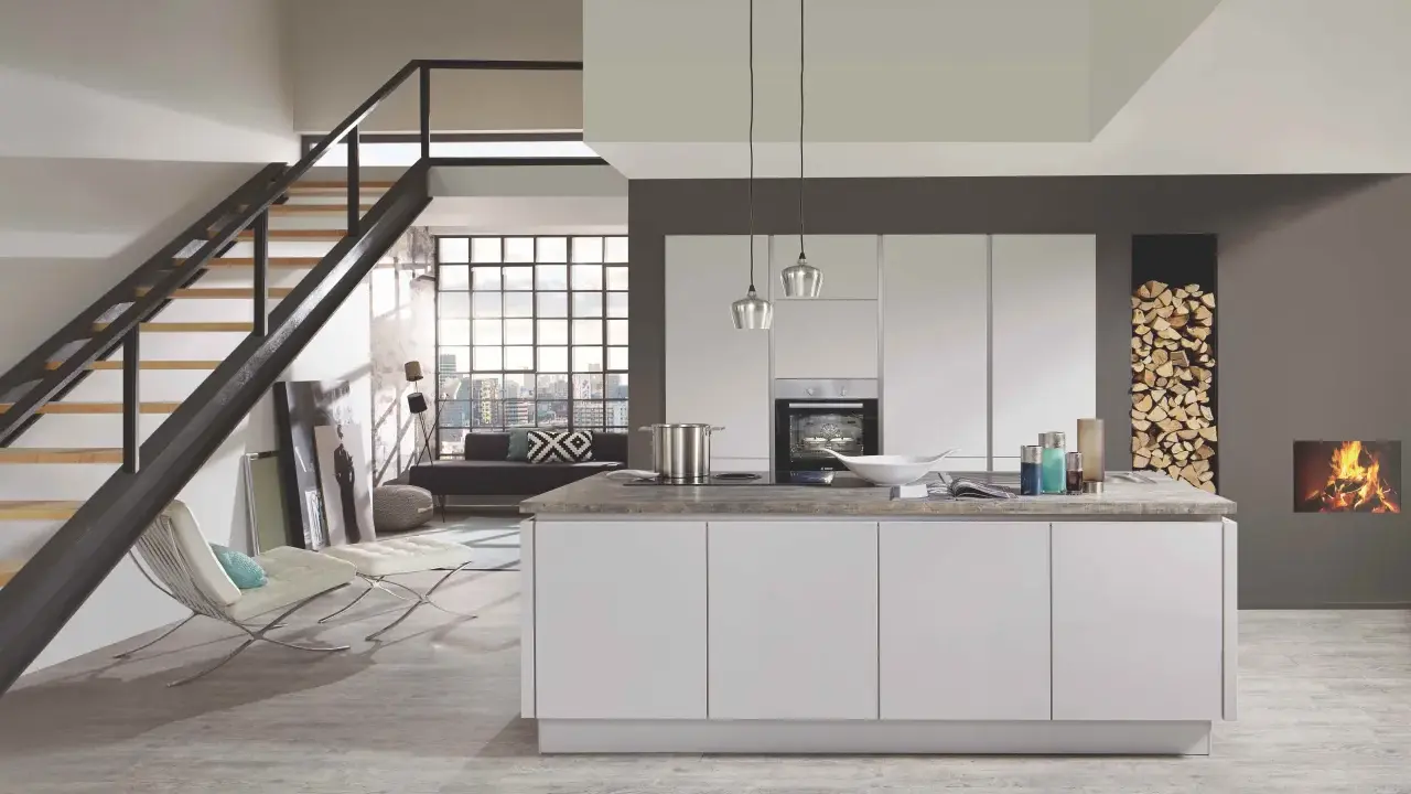 Cuisine moderne avec îlot central blanc. Le mur gris foncé contraste avec les meubles blancs et le bois de chauffage.