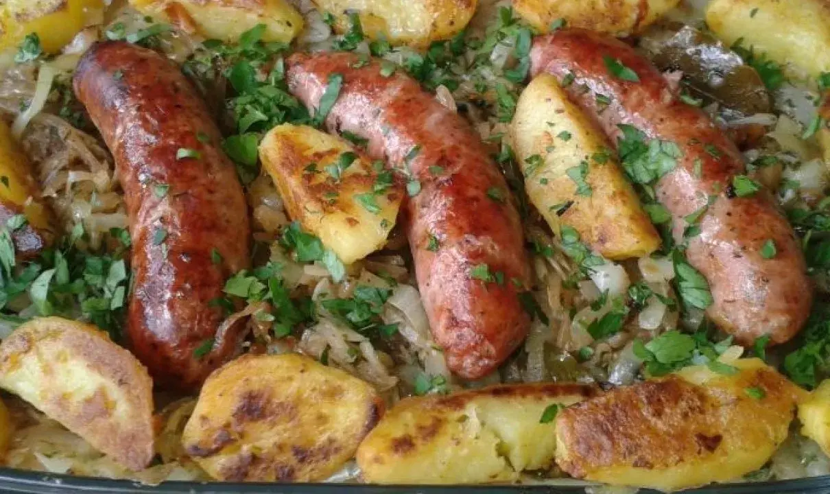 Pyszna biała kiełbasa z kapustą kiszoną i pieczonymi ziemniakami, posypana natką pietruszki.