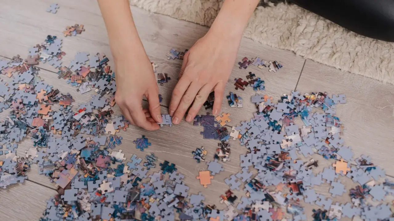 Ręce układają puzzle na podłodze. Po skończeniu dowiesz się, jak powiesić puzzle na ścianie.