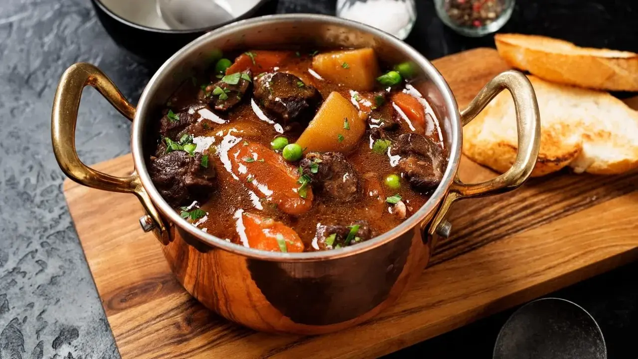 Herzhaftes Chili con Carne in Kupfertöpfchen, mit Kartoffeln, Karotten und Erbsen, serviert mit Baguette.