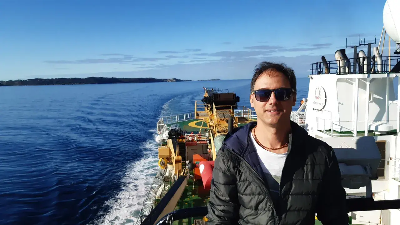 Uomo su nave, con mare e terra all'orizzonte. Un vero oceanografo significato, immerso nella sua ricerca.