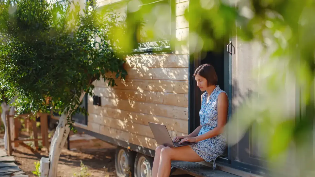 Frau arbeitet auf Laptop vor einem Tiny House. Ein Beispiel für modernes, flexibles wohnen in der zukunft.