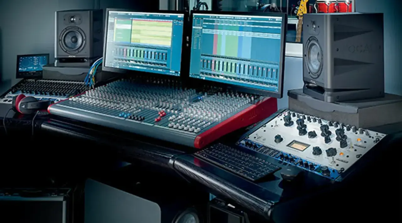 Station de mixage audio avec deux écrans, enceintes, casque et console de mixage.