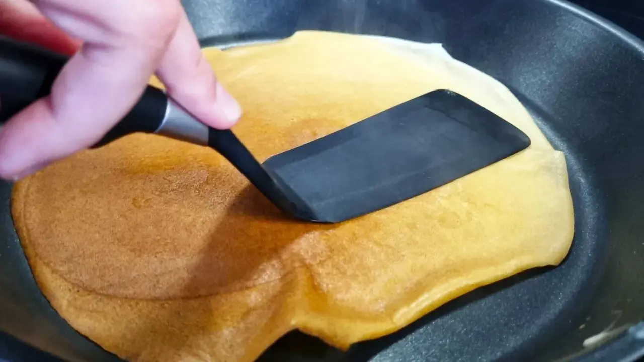 Volteando un crepé dorado en una sartén, preparado fácilmente con crepes thermomix.