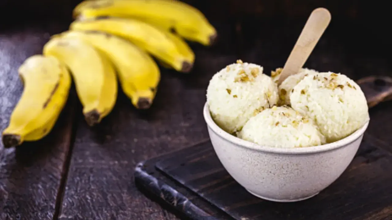Delicioso helado de plátano cremoso, adornado con nueces, junto a racimos de plátanos frescos sobre una mesa de madera rústica.