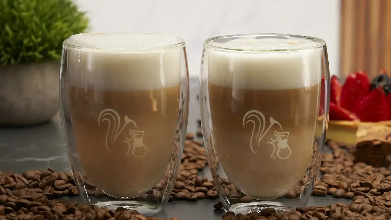 Zwei Latte Macchiato im Glas, umgeben von Kaffeebohnen. Ein typischer Latte Macchiato hat ca. 250-300 ml.