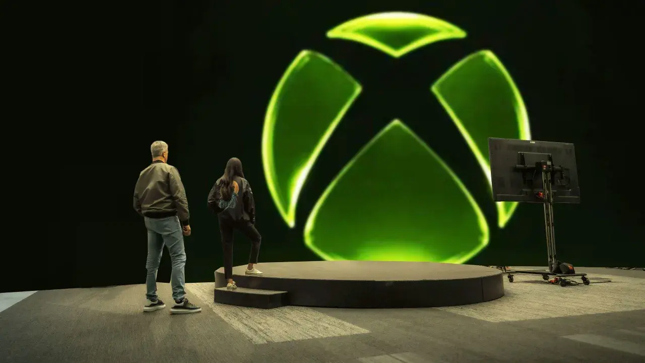 Osoby stoją przed wielkim zielonym logo Xbox. Czy to zapowiedź nowej gry, czy może Xsolla co to za platforma?
