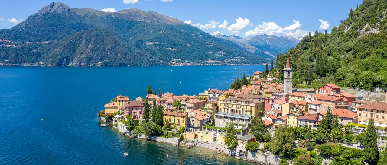 Färgstarka hus vid en azurblå sjö, omgivna av gröna berg. Ett perfekt exempel på mysiga resmål i Italien.