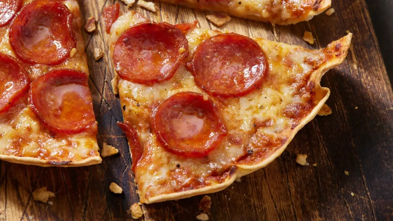 Pyszna pizza na tortilli z pepperoni, roztopionym serem i chrupiącym spodem, podana na drewnianej desce.
