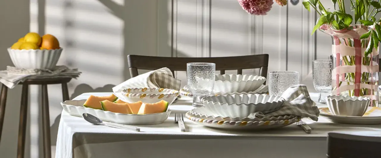 Ett dukat bord med en fin servis, frukt och blommor. Vackra vita skålar med vågiga kanter och glas med textur.