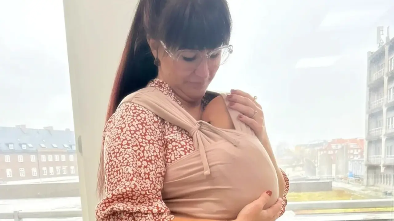 En mamma i sjal håller sitt barn nära sig.