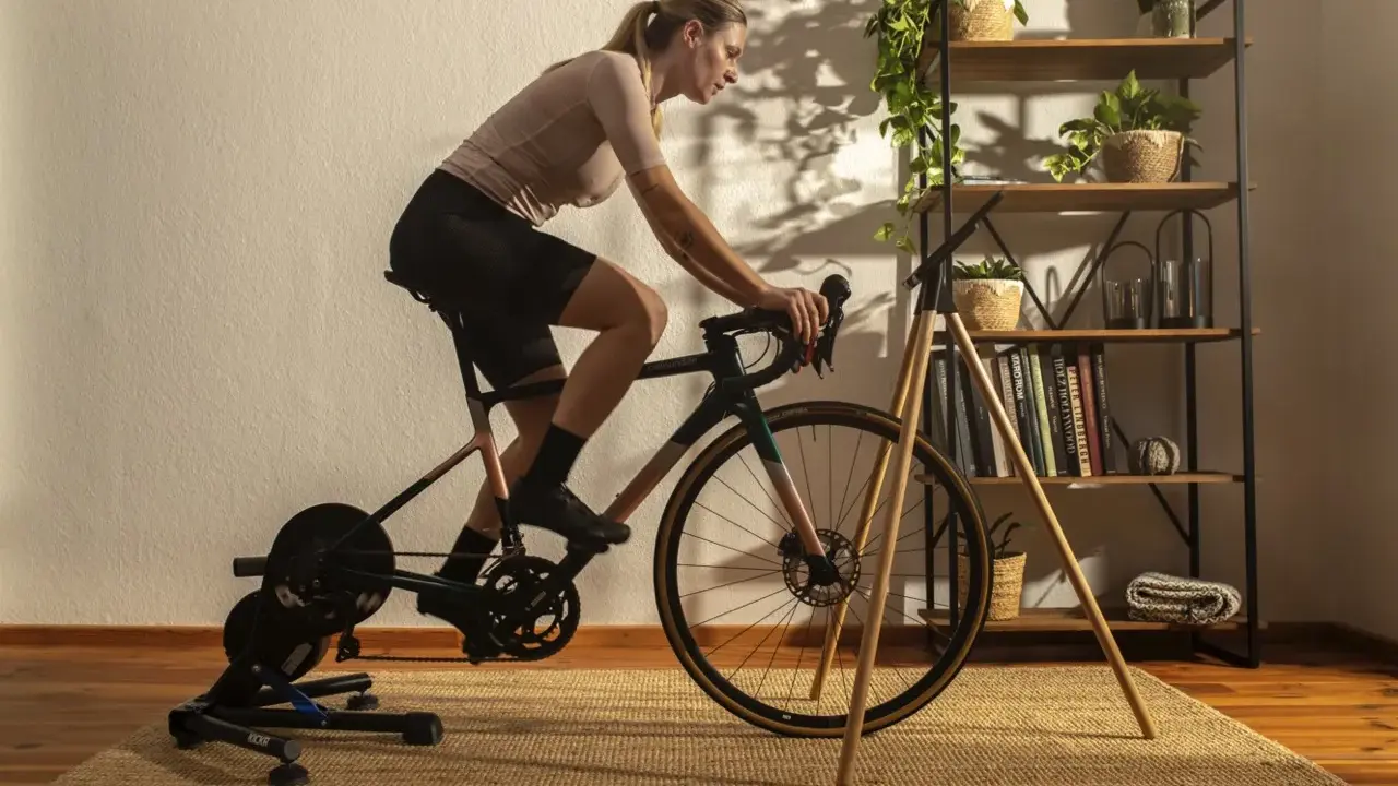 Frau trainiert auf einem Heimtrainer, was ist spinning? Sie tritt kräftig in die Pedale, während im Hintergrund ein Regal mit Pflanzen und Büchern steht.
