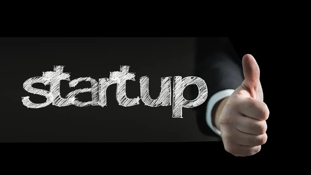 Słowo "startup" napisane kredą na czarnym tle, obok kciuk w górę. To symbol sukcesu w biznesie.