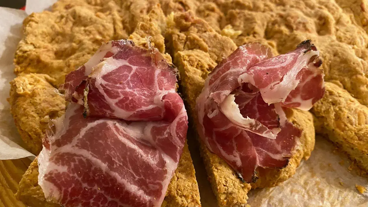 La ciaccia di Pasqua toscana, fragrante e dorata, è guarnita con fette di salume rosa.