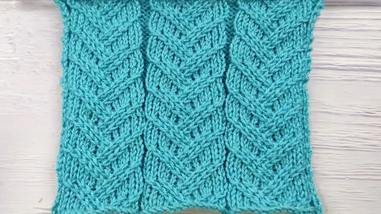 Muestra de tejido azul turquesa con patrón de espiga en dos agujas. Las hebras forman un diseño entrelazado que recuerda a espigas de trigo.