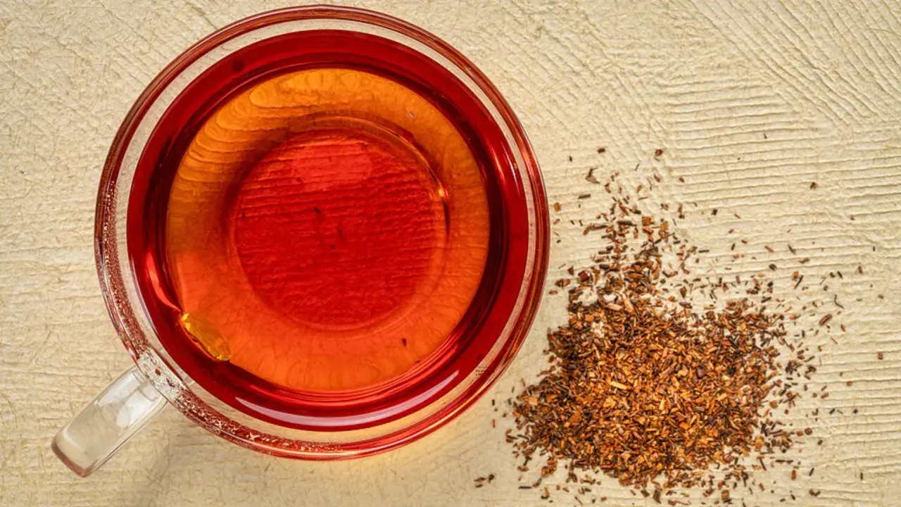 Eine Tasse roter Rooibos Tee neben getrockneten Blättern. Ideal für die Schwangerschaft.