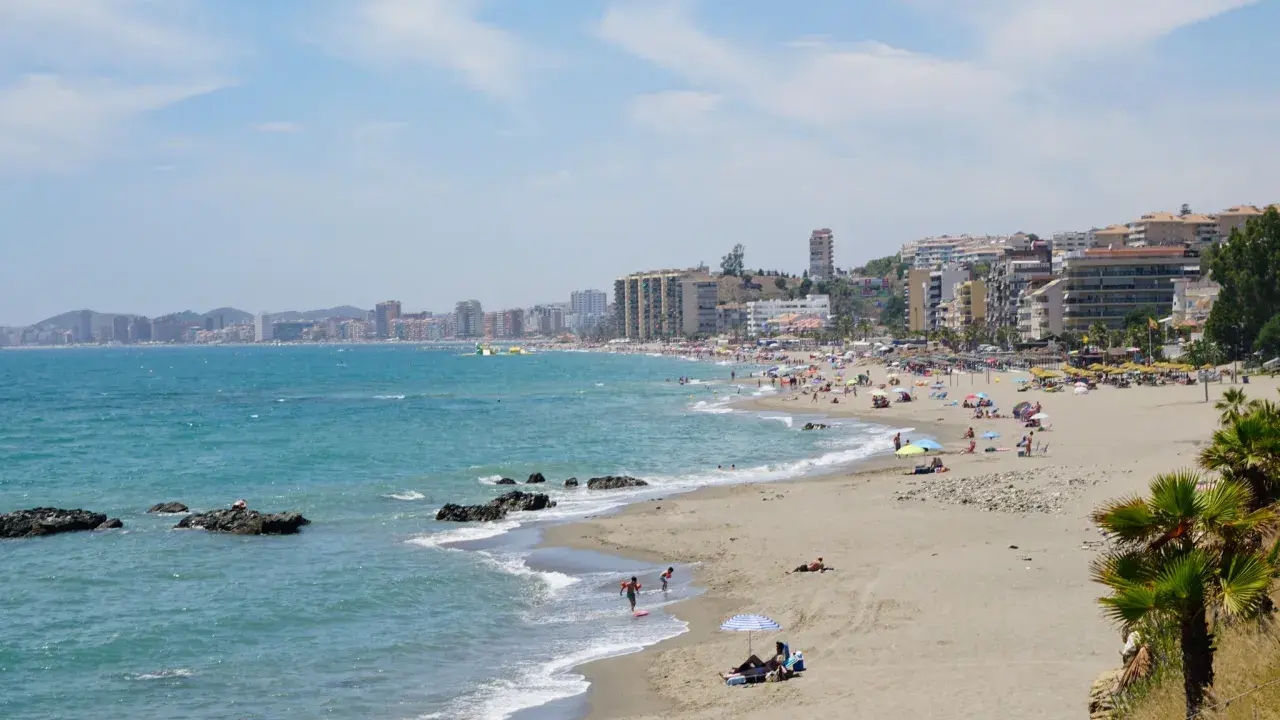 Sonniger Benalmadena Strand mit vielen Menschen, bunten Sonnenschirmen und dem türkisfarbenen Meer.
