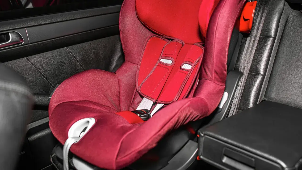 Silla de coche roja en asiento de cuero negro. Las sillas Isofix se pueden poner con cinturón, ofreciendo versatilidad para la seguridad infantil.
