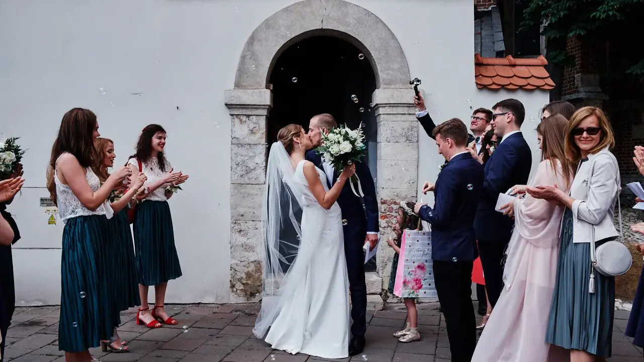 Para młoda całuje się przed kościołem, goście sypią bańki mydlane. To piękny ślub jednostronny, przysięga miłości.