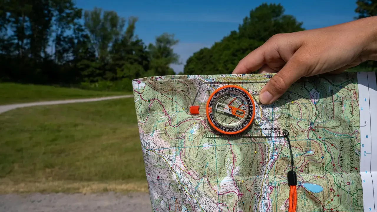 Dłoń trzyma mapę i kompas, pokazując, jak działa kompas w terenie.