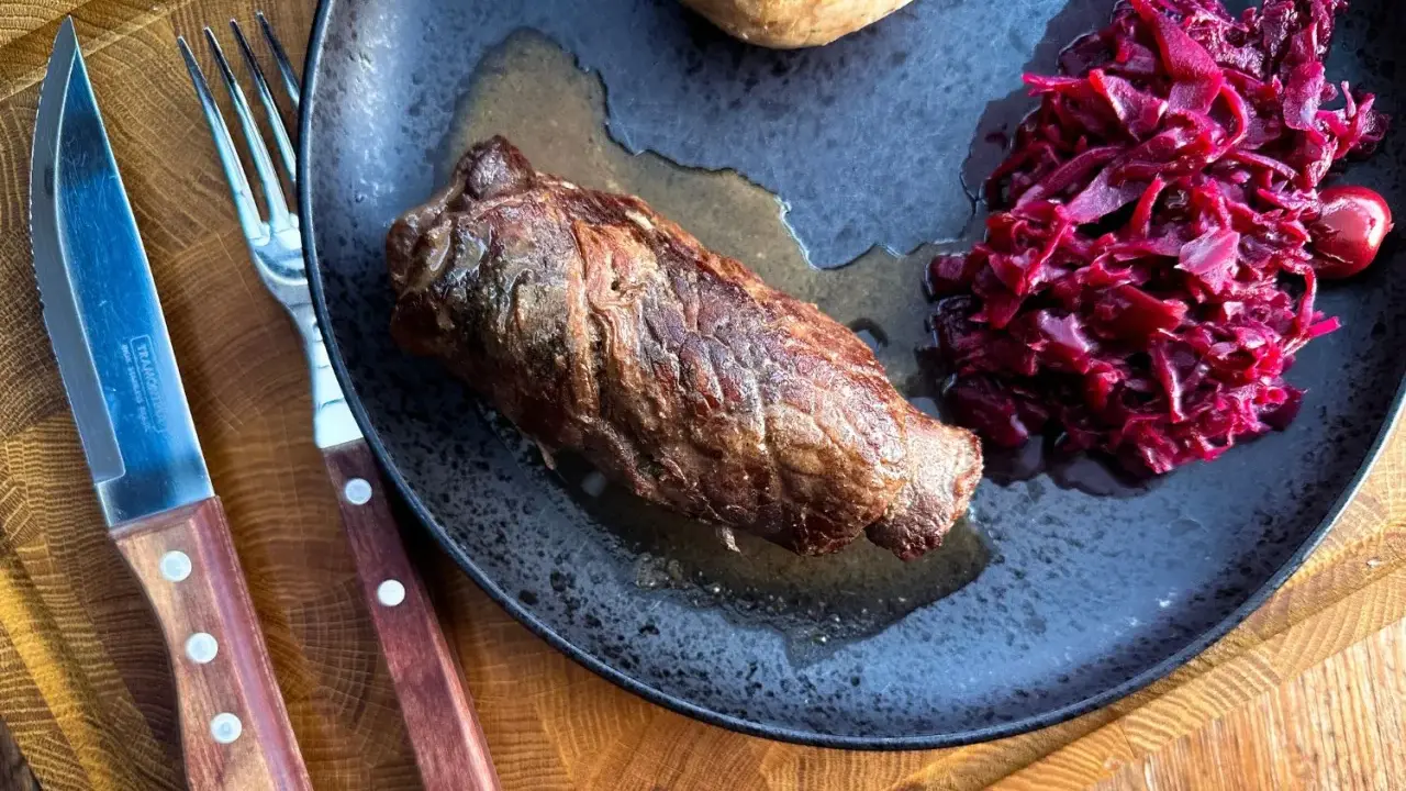 Herzhafte Rouladen im Dutch Oven zubereitet, serviert mit Rotkohl und Klößen auf einem rustikalen Teller.