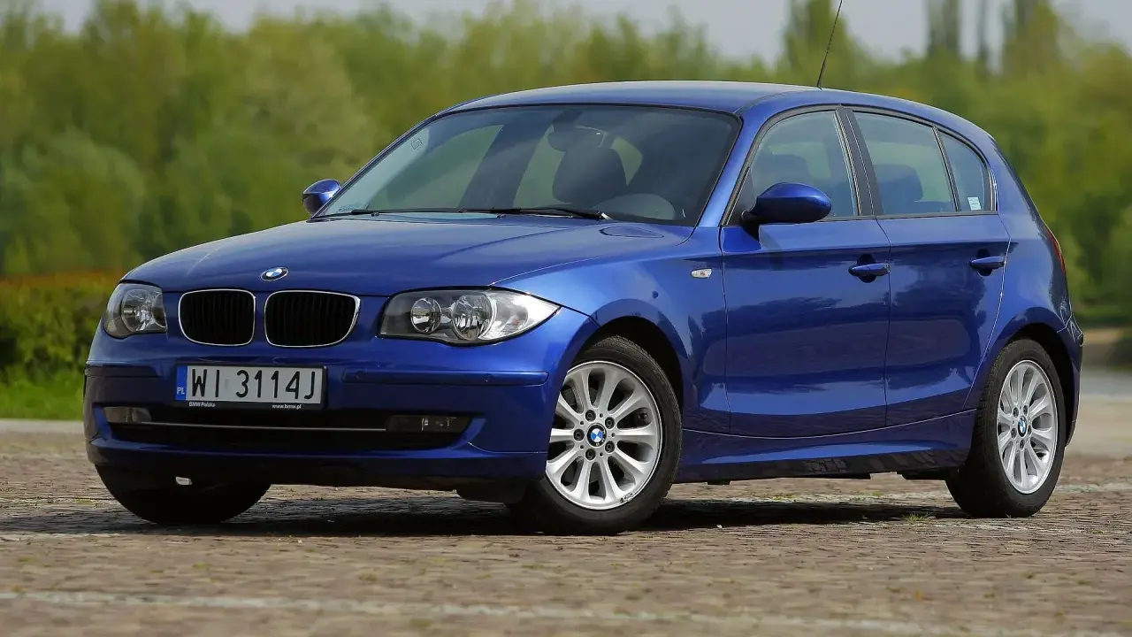 Niebieskie BMW 118i na tle zieleni. Elegancki hatchback z polskimi tablicami rejestracyjnymi WI 3114J.