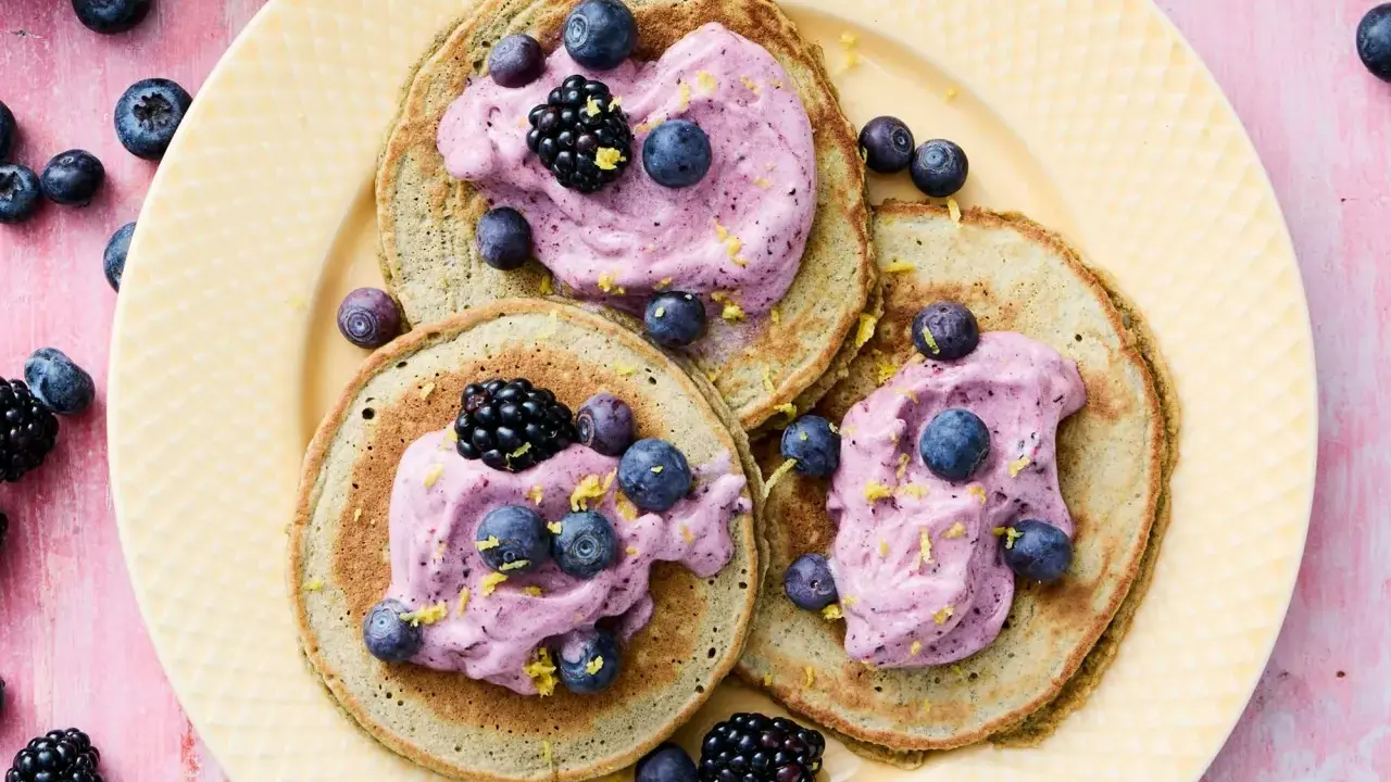 Tre fluffiga pannkakor med havregryn toppas med lila grädde, blåbär och björnbär. Strössel av citronskal ger en frisk touch.