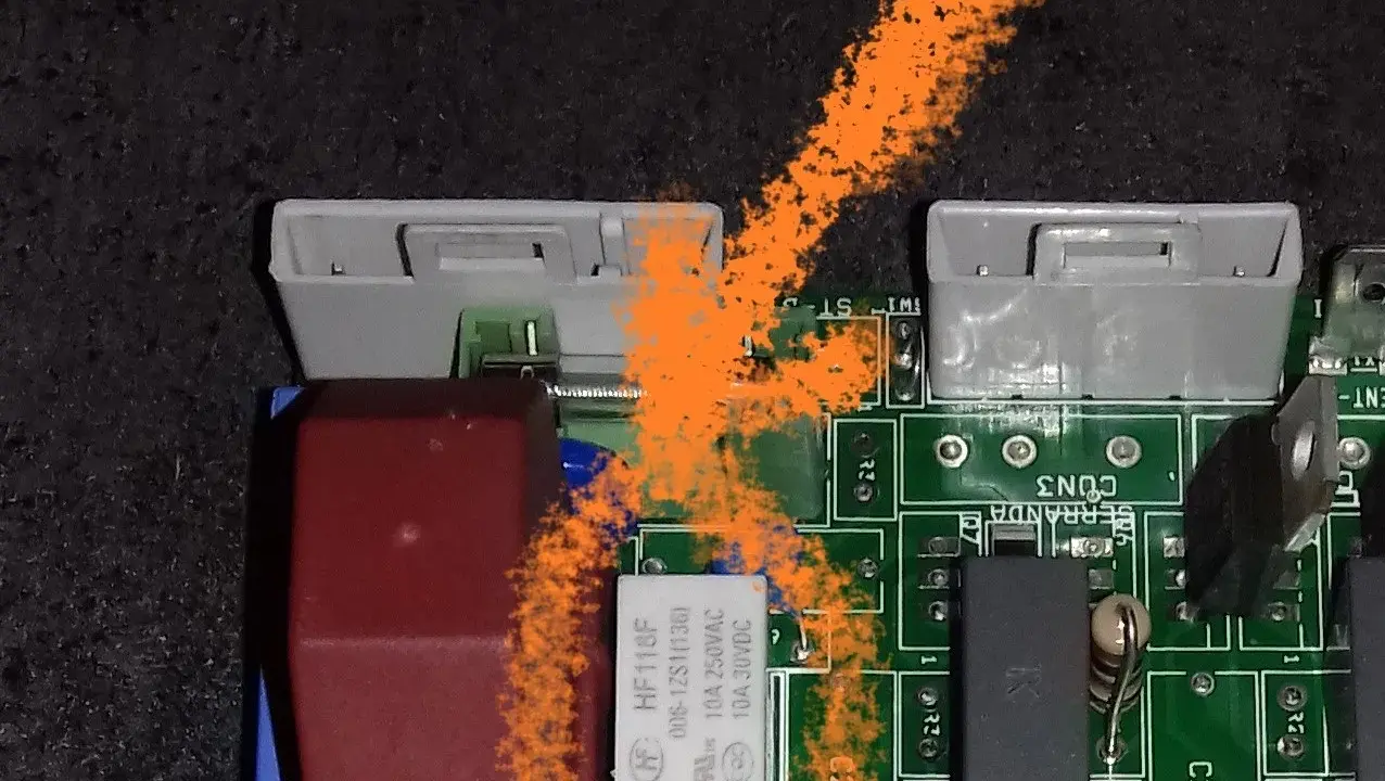 Carte mère de poêle à granulés avec un problème. On voit des connecteurs, des composants électroniques et une trace orange.