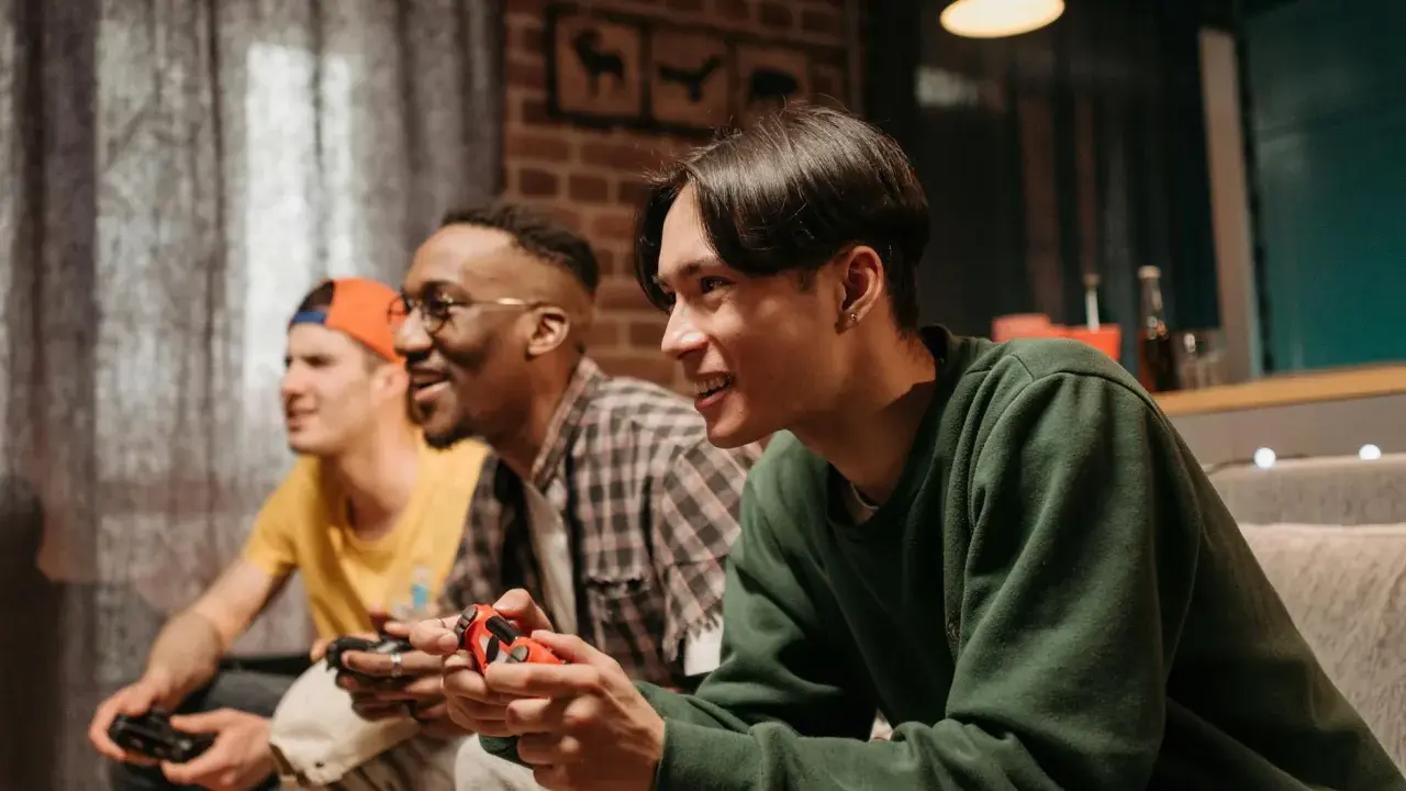 Trzech przyjaciół gra w darmowe gry na PS4, śmiejąc się i rywalizując.