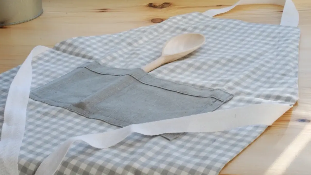Gotowy fartuch kuchenny w kratkę, z drewnianą łyżką w kieszeni. Idealny poradnik, jak uszyć fartuch kuchenny.