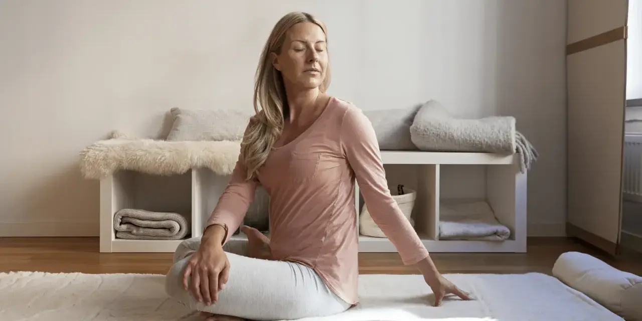 Kvinna i rosa tröja och grå byxor gör en vridning i sittande ställning, en form av gående meditation.