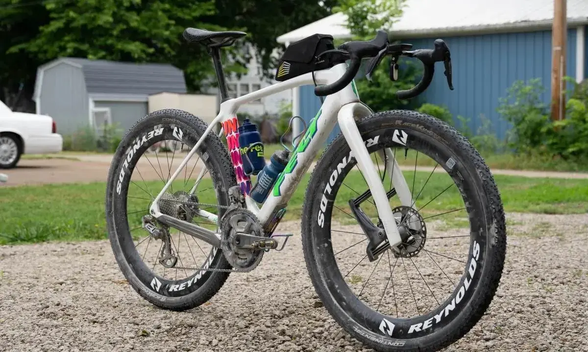 Biały rower gravelowy z szerokimi oponami i sakiewką na kierownicy, gotowy na przygodę. Czy to gravel czy szosa, zależy od terenu!