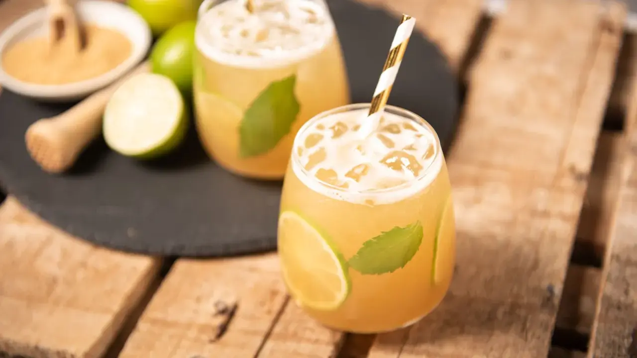 Erfrischender cocktail mit braunem rum, Limette und Minze, serviert mit Eis und einem gestreiften Strohhalm.