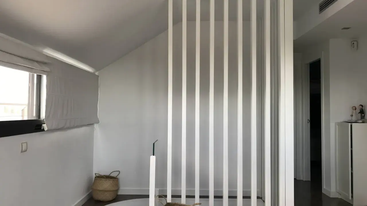 Modern interior with a white slatted partition, possibly to tirar tabique para unir dos pisos. Baskets and a window are visible.