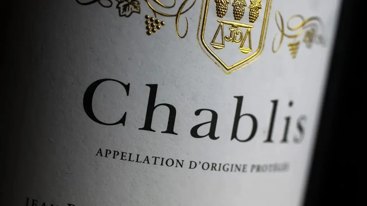 Nahaufnahme eines Etiketts mit der Aufschrift "Chablis". Ein goldenes Wappen mit Trauben und Waage ziert das Etikett dieses Chablis Weins.