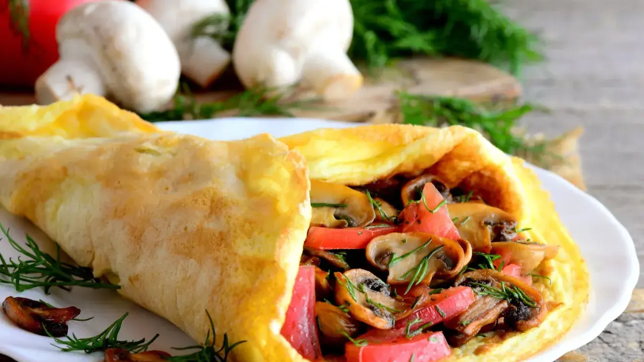 Złocisty omlet z pomidorami i pieczarkami, udekorowany koperkiem. Pyszne śniadanie na drewnianym blacie.