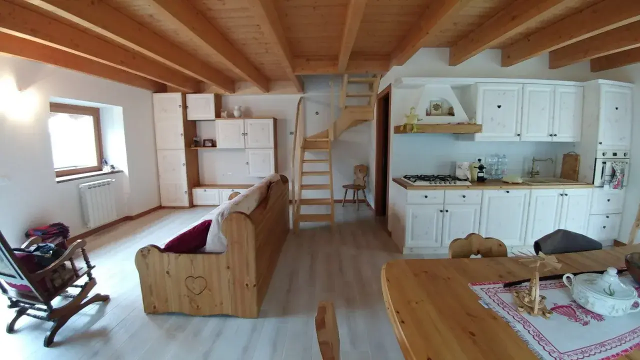 Come arredare una taverna: cucina bianca, divano in legno, scala a vista e soffitto a travi.