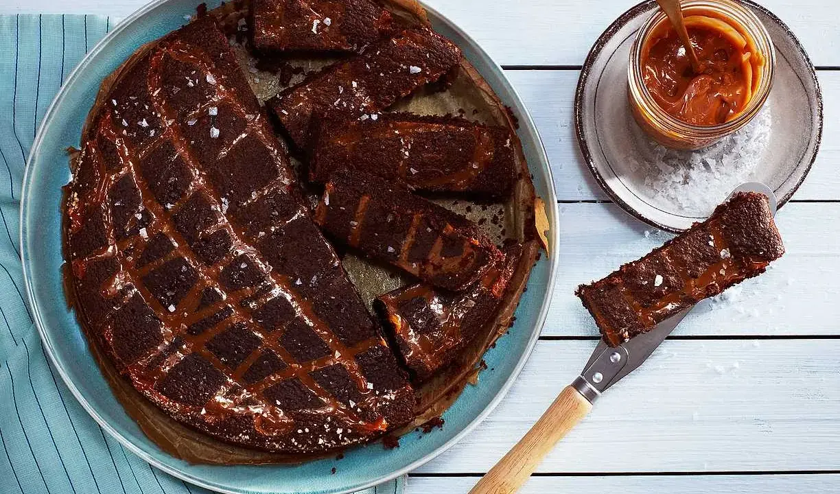Chokladkaka med kolasås och havssalt, perfekt att baka glutenfritt. En bit lyfts upp med en kniv.