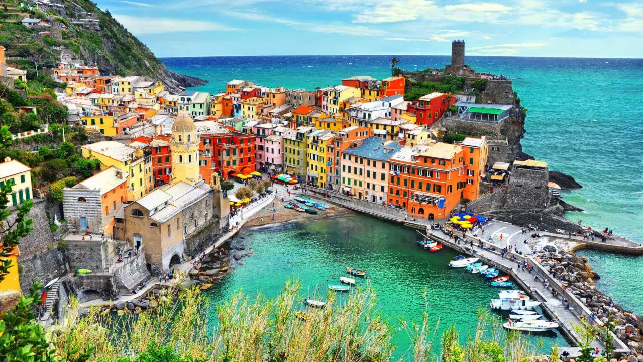 Vernazza, una delle Cinque Terre, con case colorate a picco sul mare turchese e un porticciolo pieno di barche.