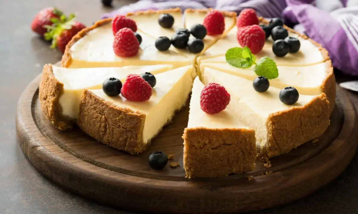 Pyszna tarta sernikowa z malinami i borówkami na drewnianej desce.