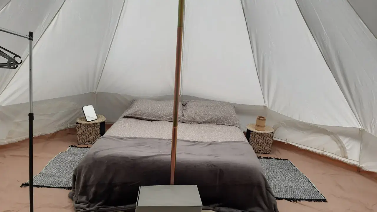Komfortowy glamping nad morzem: łóżko z pościelą, stoliki nocne, wieszak i namiot.