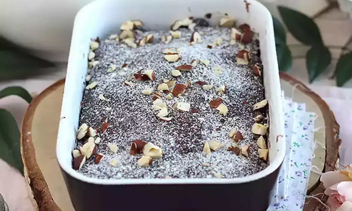 Pyszny brownie z mikrofali, posypany cukrem pudrem i orzechami, w białej ceramicznej formie.