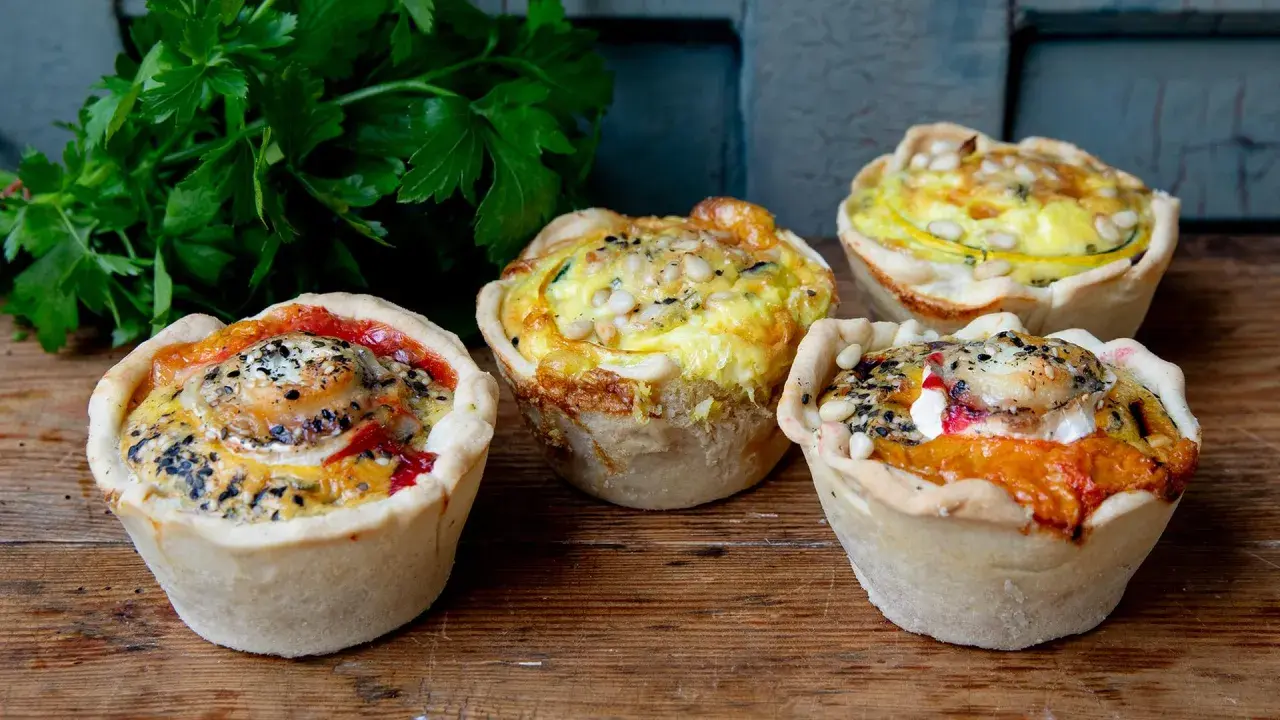 Vier köstliche Mini-Quiches mit verschiedenen Füllungen, perfekt für ein schnelles mini quiche rezept. Mit Petersilie garniert.
