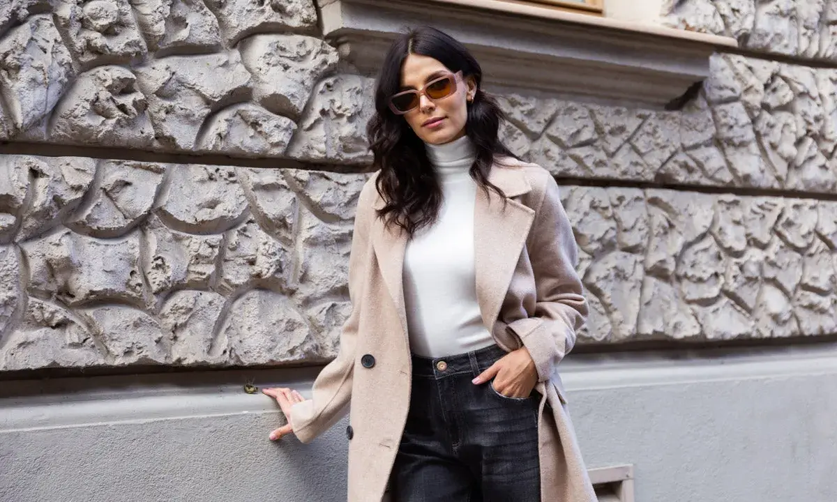 Elegancka kobieta w beżowym płaszczu i ciemnych jeansach. Spódnica jeansowa midi stylizacje na co dzień.